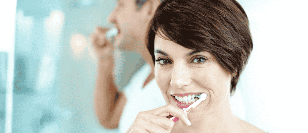 Woman brushing her teeth to care for full arch dental implants