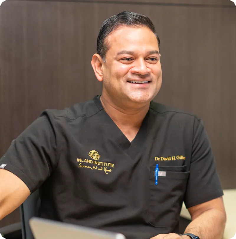 Dr. David H. Gilbert smiling at his desk in surgical scrubs